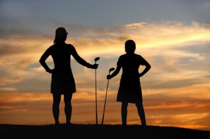 Silhouette of two women standing with golf clubs in their hands